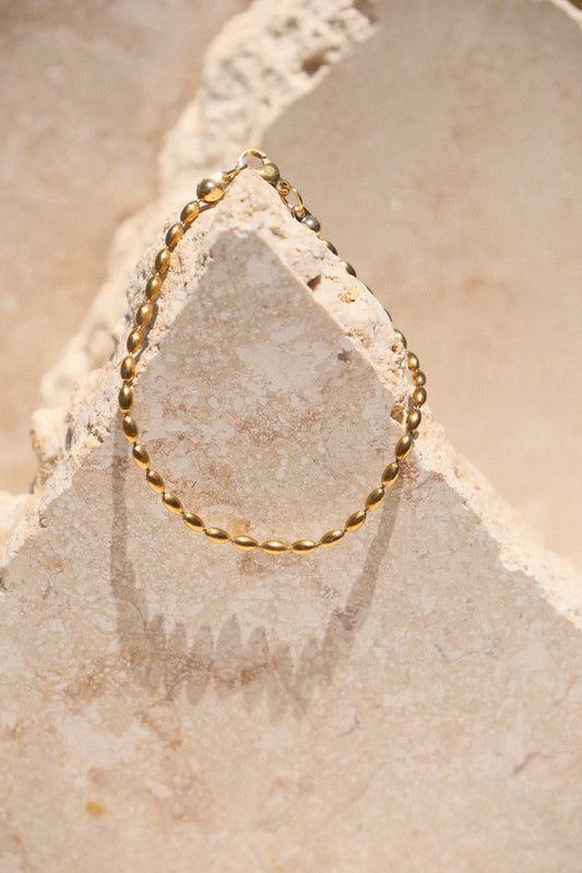 Sol & Aura - Minnie Bracelet - Gold beaded chain bracelet on a textured stone surface