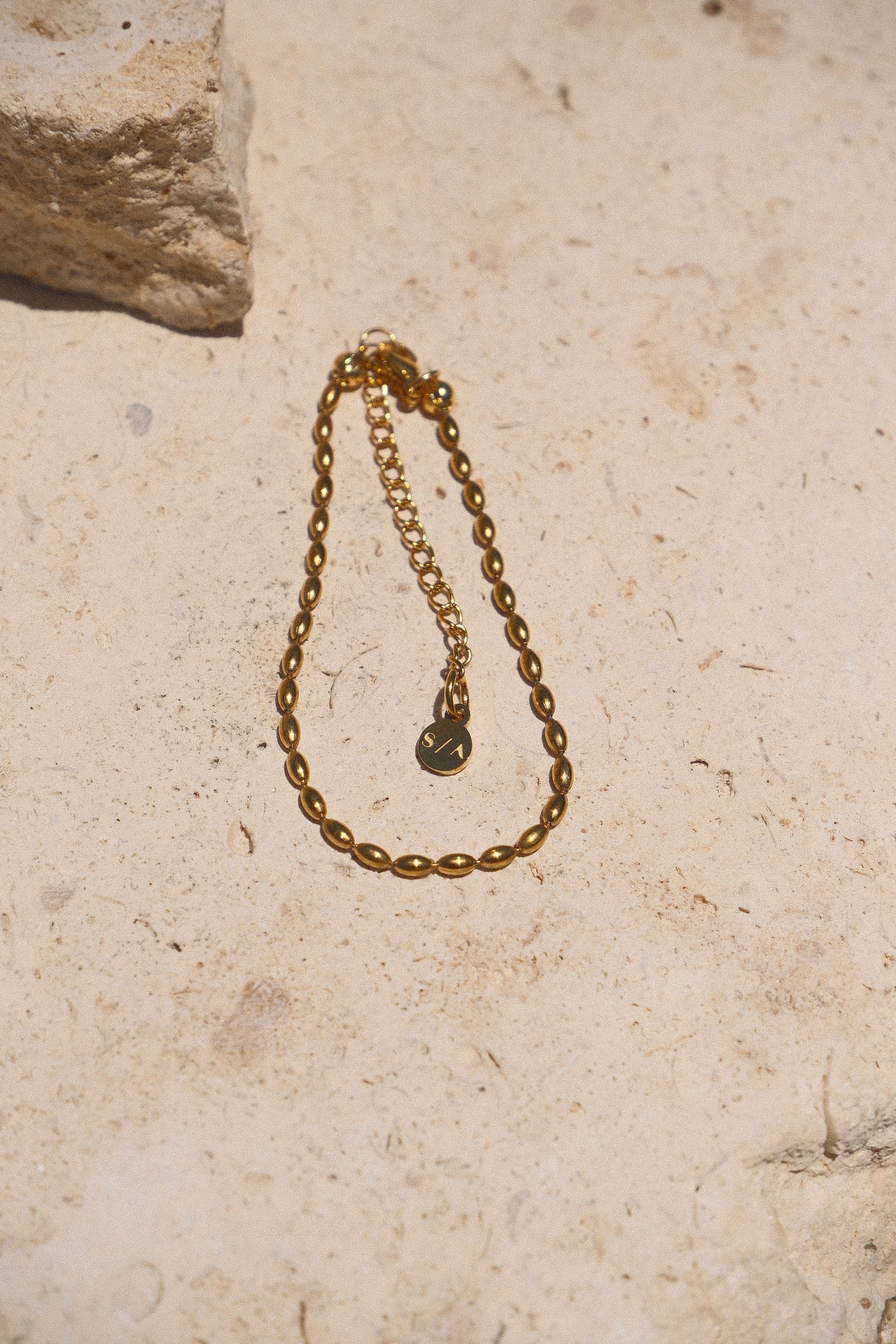 Sol & Aura - Minnie Bracelet - Gold beaded chain bracelet on a textured stone surface