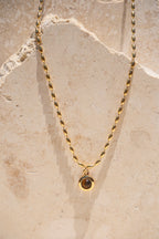 Sol & Aura - Minx Necklace. Brown pendant Tiger's Eye pendant on gold beaded chain hanging off stone surface