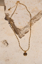 Sol & Aura - Minx Necklace. Brown pendant Tiger's Eye pendant on gold beaded chain lying on stone surface