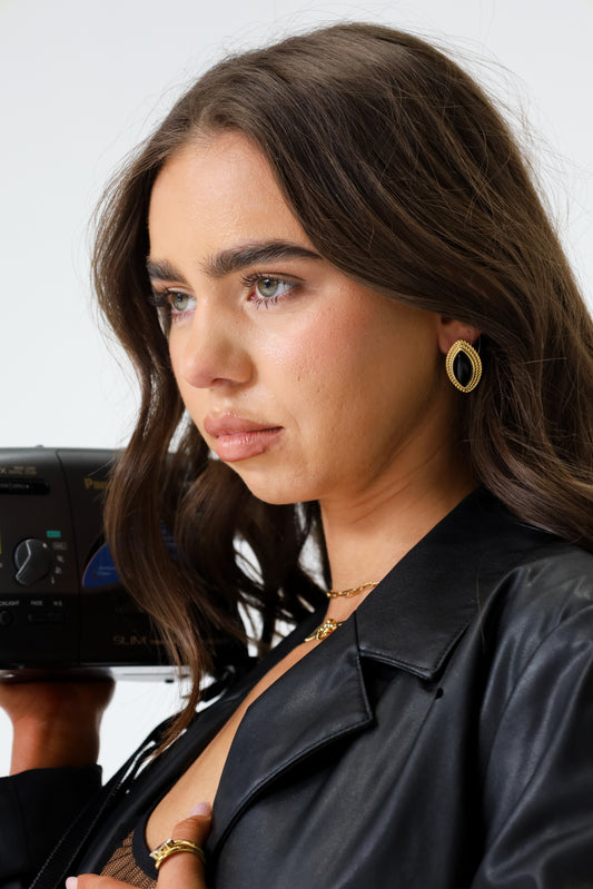 Sol & Aura - PHARAOH Earrings in black on woman wearing black lather jacket, holding vintage camera recorder with long dark hair