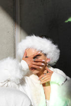 Person wearing a white fur coat and hat with a blurred background