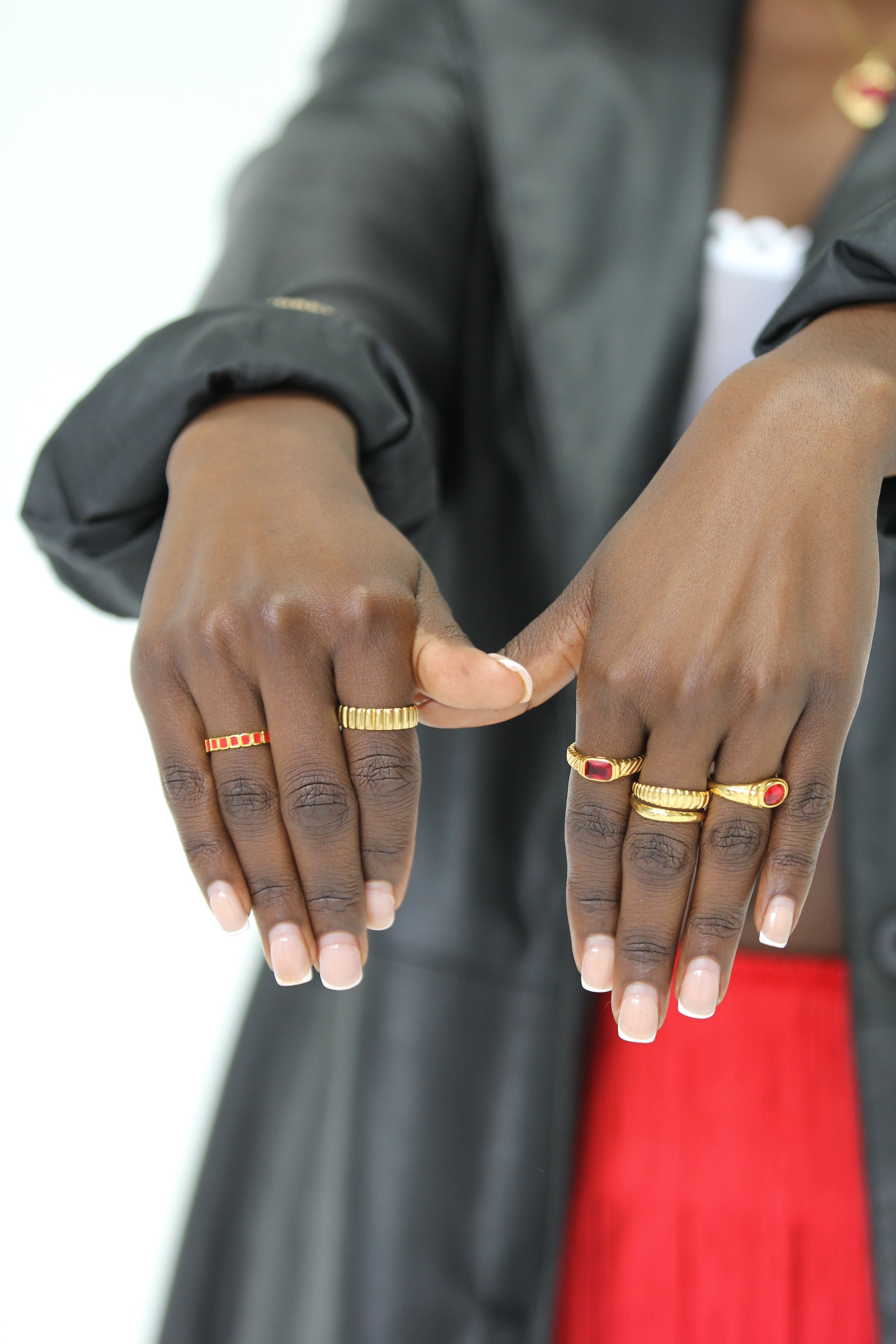 Close-up of hands with rings on fingers, wearing a black jacket and red garment.