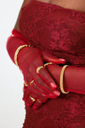 Sol & Aura - RUMI Ring, DIVINE Ring, MUSE Bangle, JANA Bangle in gold on woman's hand wearing red lace outfit and red sheer gloves against white background 
