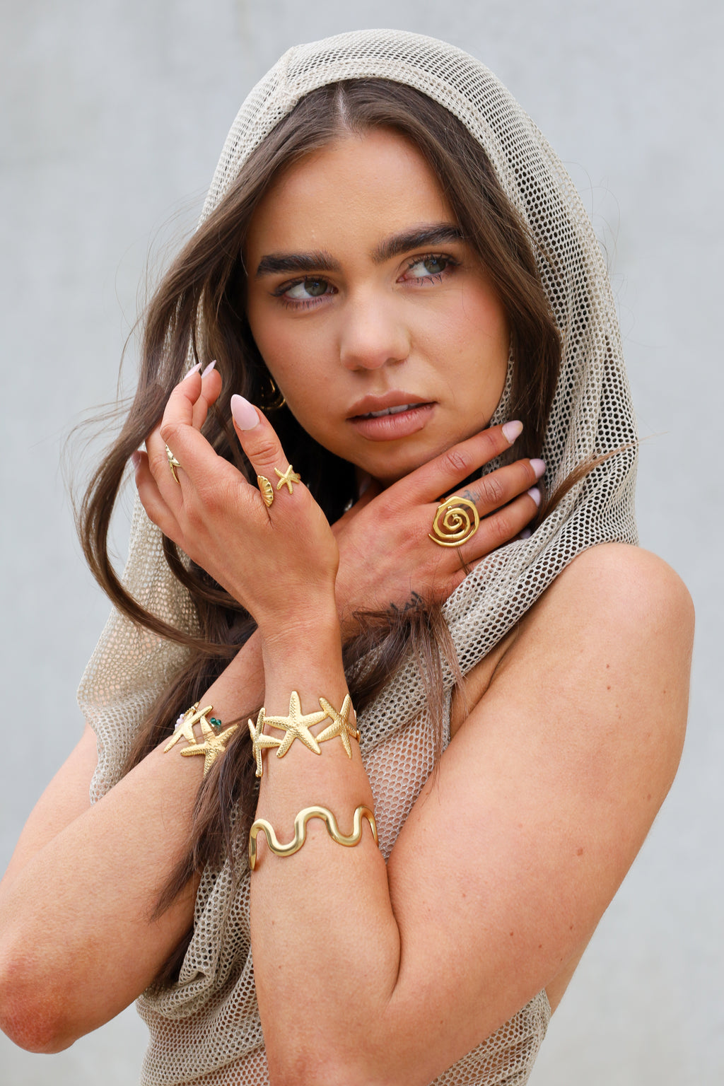 Sol & Aura - SIA Ring, ESSIE Ring, STEVIE Bangle, LOLA Bangle in Gold on woman's hands and fingers wearing mesh top and dark hair