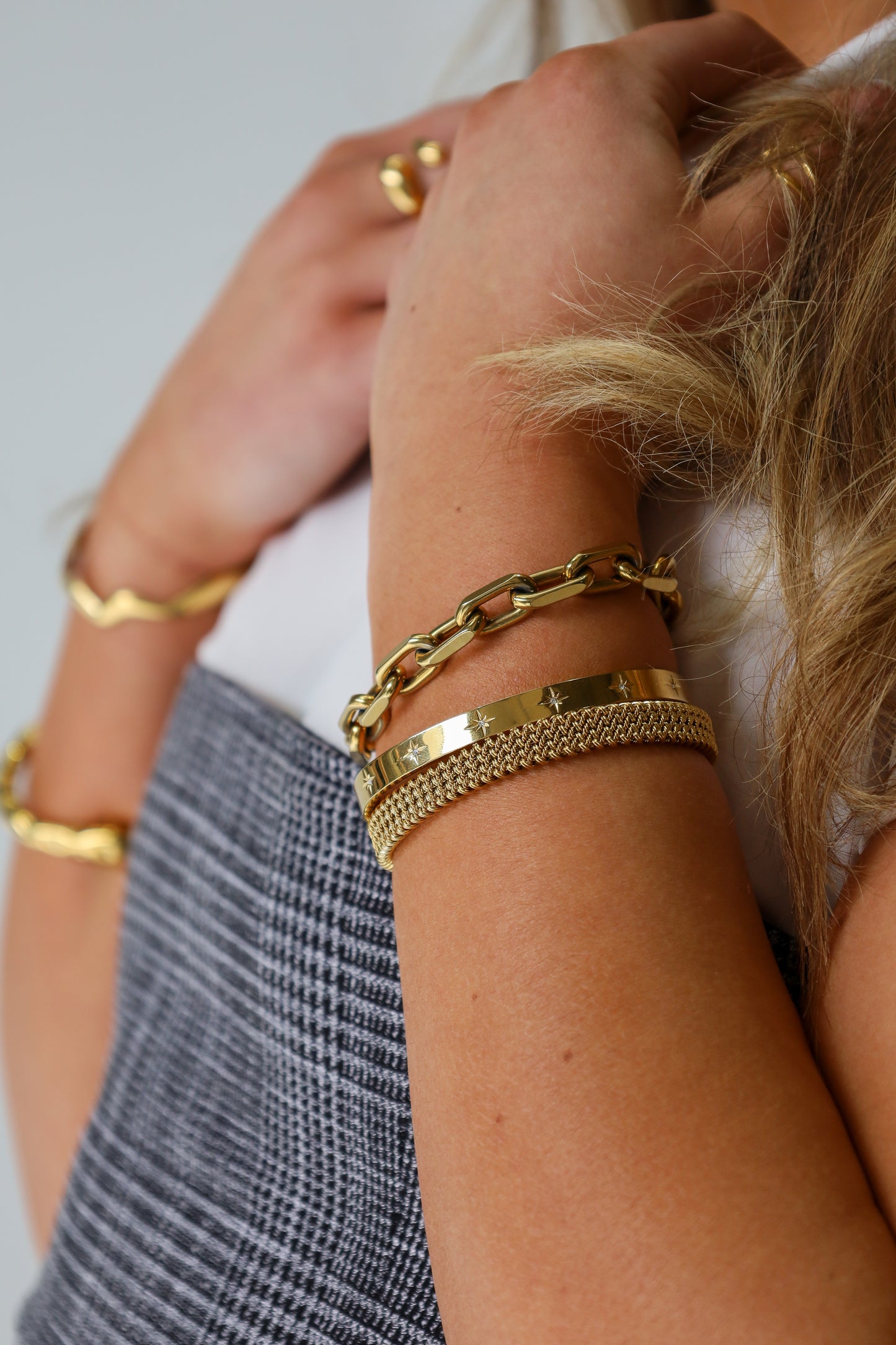 Sol & Aura - Close-up of woman's arm wearing multiple gold plated waterproof hypoallergenic Sol & Aura bracelets on a neutral background