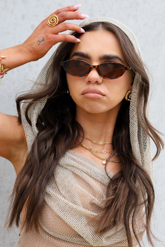 Sol & Aura - Sicily Sunglasses with tortoise shell detailing and Essie Ring in gold on woman in mesh hooded top
