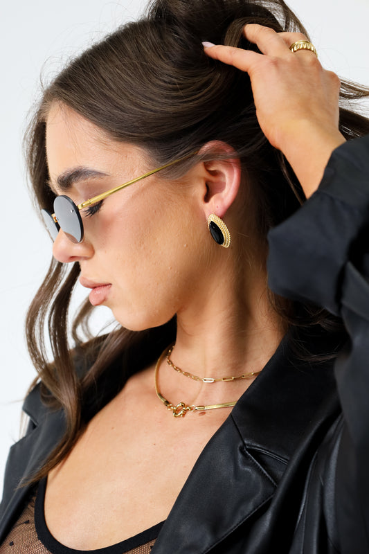 Sol & Aura - Side view of MILLENIA Sunglasses and PHARAOH Earrings in Black on woman wearing black leather jacket and lace bralette against white background