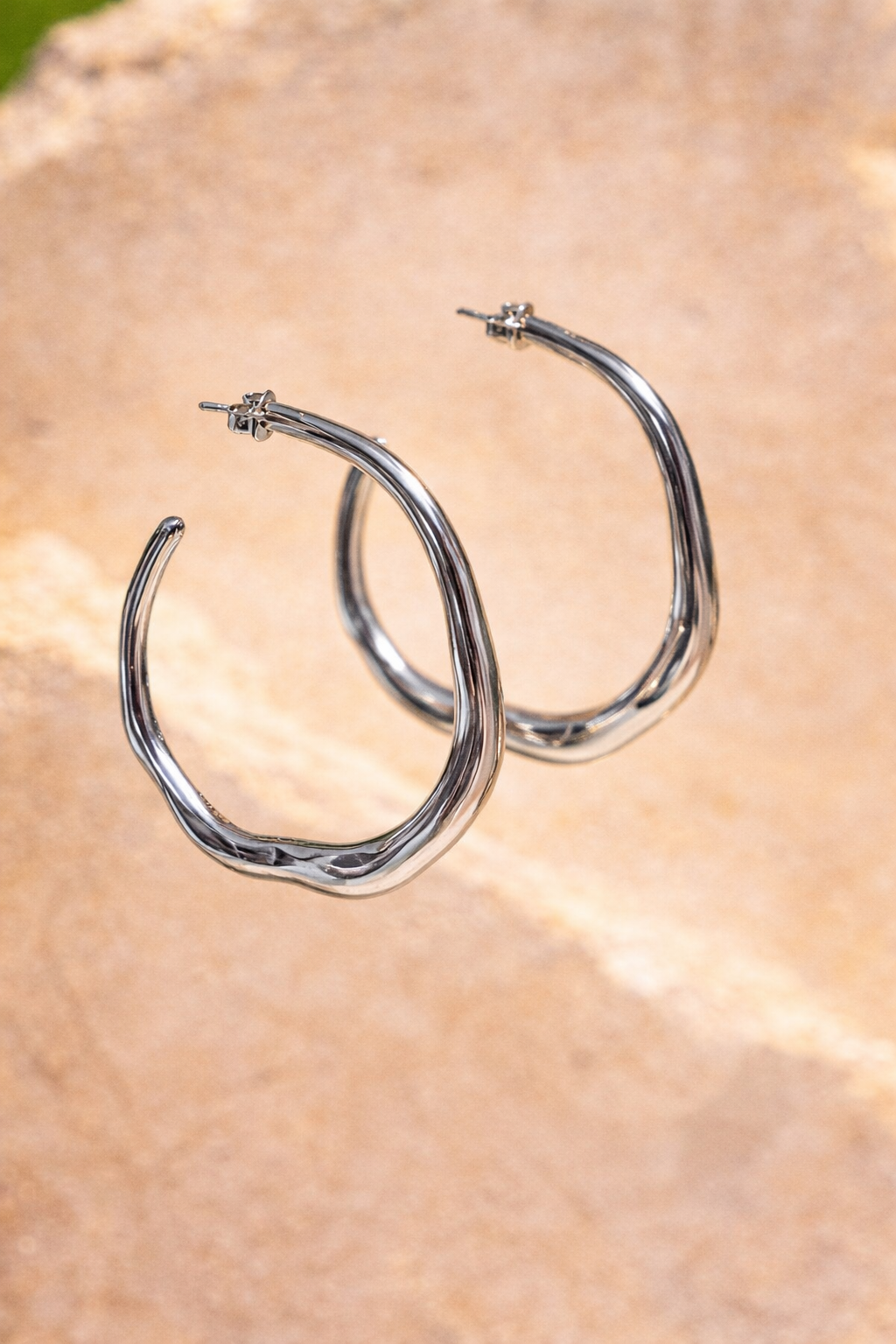 Sol & Aura - Silver hoop earrings hanging in front of a stone surface