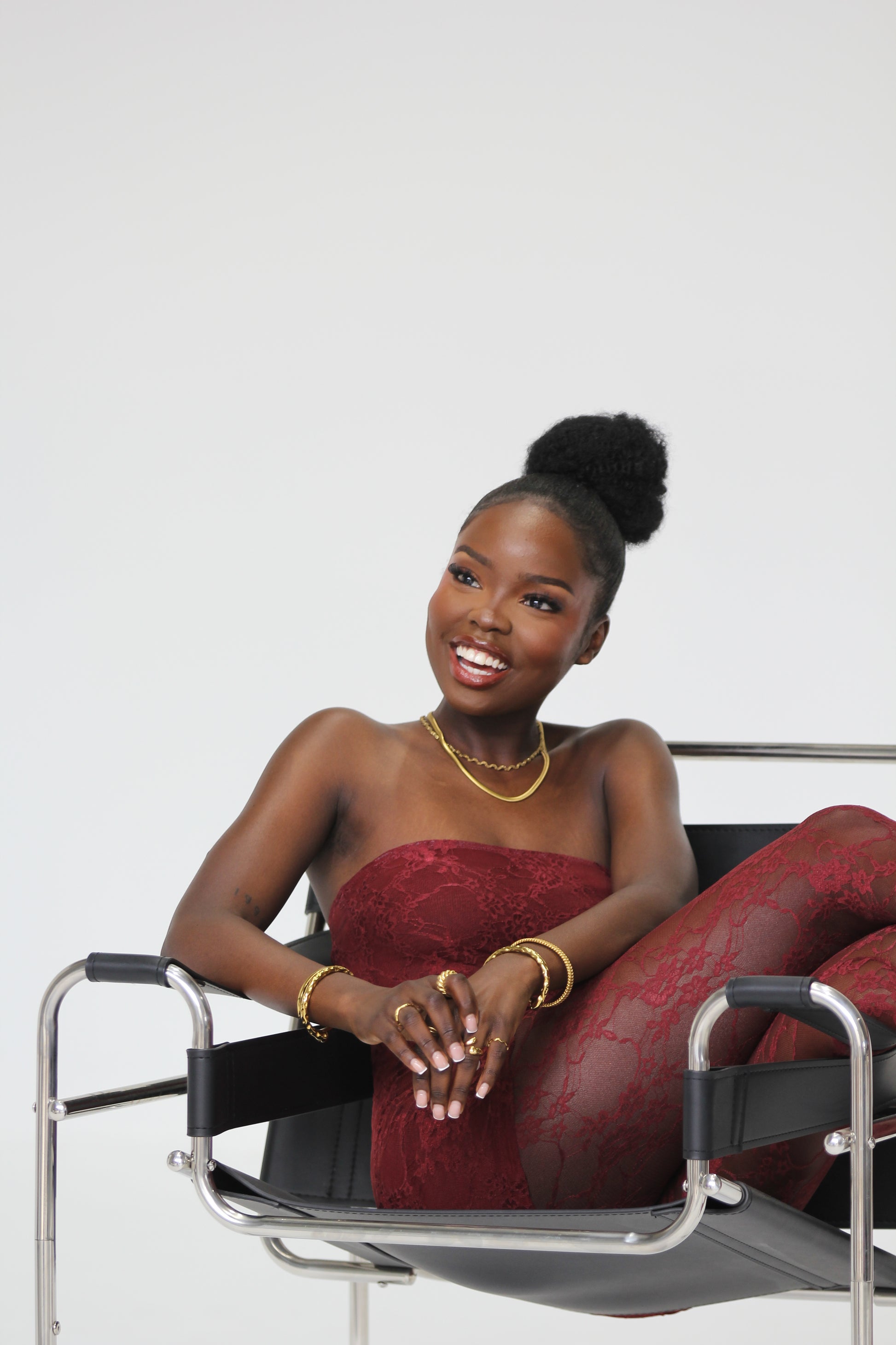 Sol & Aura - smiling woman wearing gold plated hypoallergenic waterproof jewellery in red lace outfit sitting on modern chair