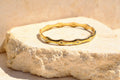 Sol & Aura - Wavy gold bracelet with gemstone star accents on a textured stone surface