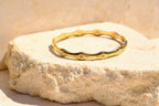 Sol & Aura - Wavy gold bracelet with gemstone star accents on a textured stone surface