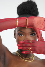 Sol & Aura - Muse Bangle, Ripple RIng, Reign Ring - Woman framing face with hands in red mesh gloves & gold Sol & Aura jewellery